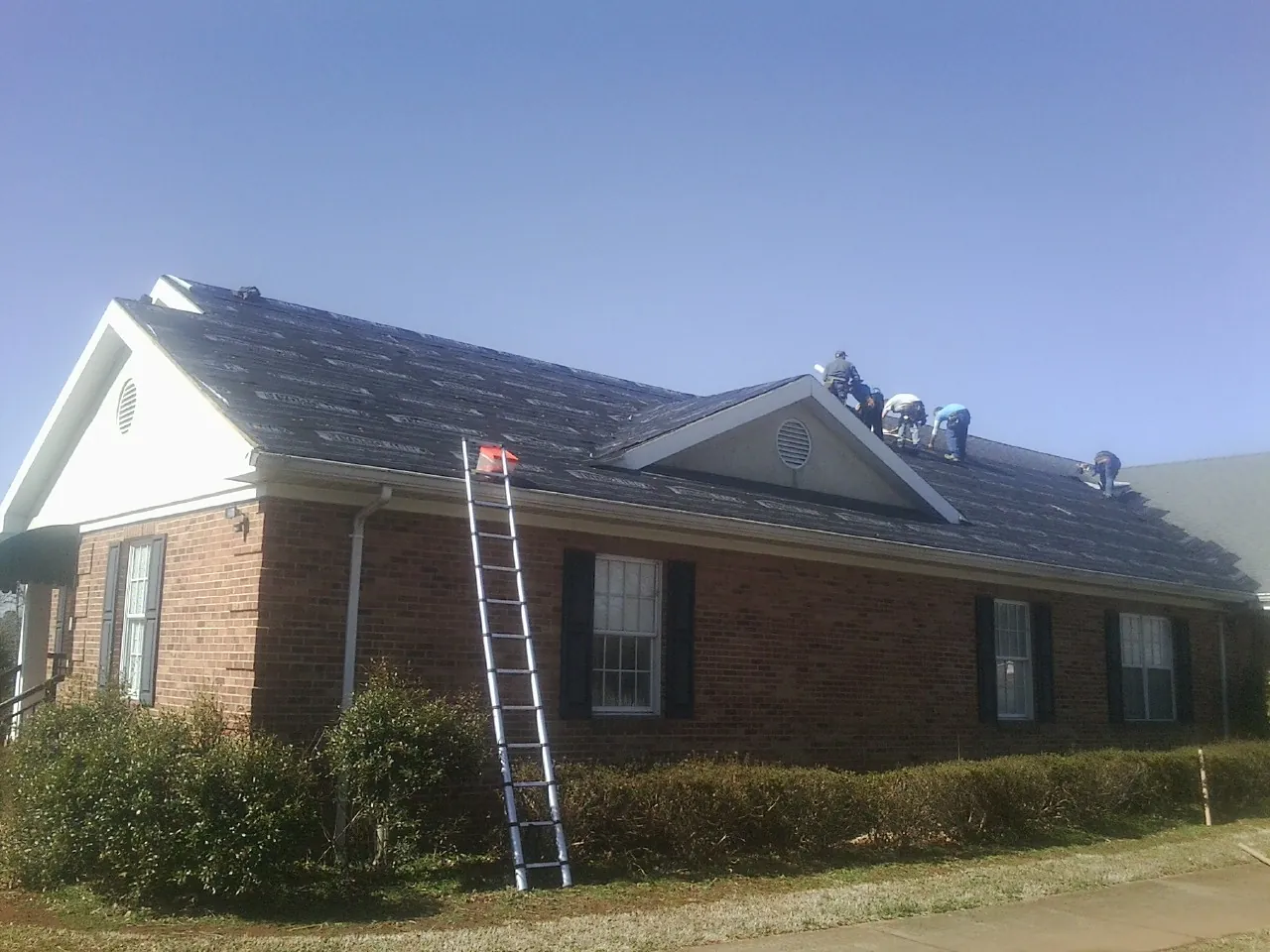 Crew tearing shingles off a brick ranch roof with a ladder set — Emergency Roof Repair work by our crew in Covesville