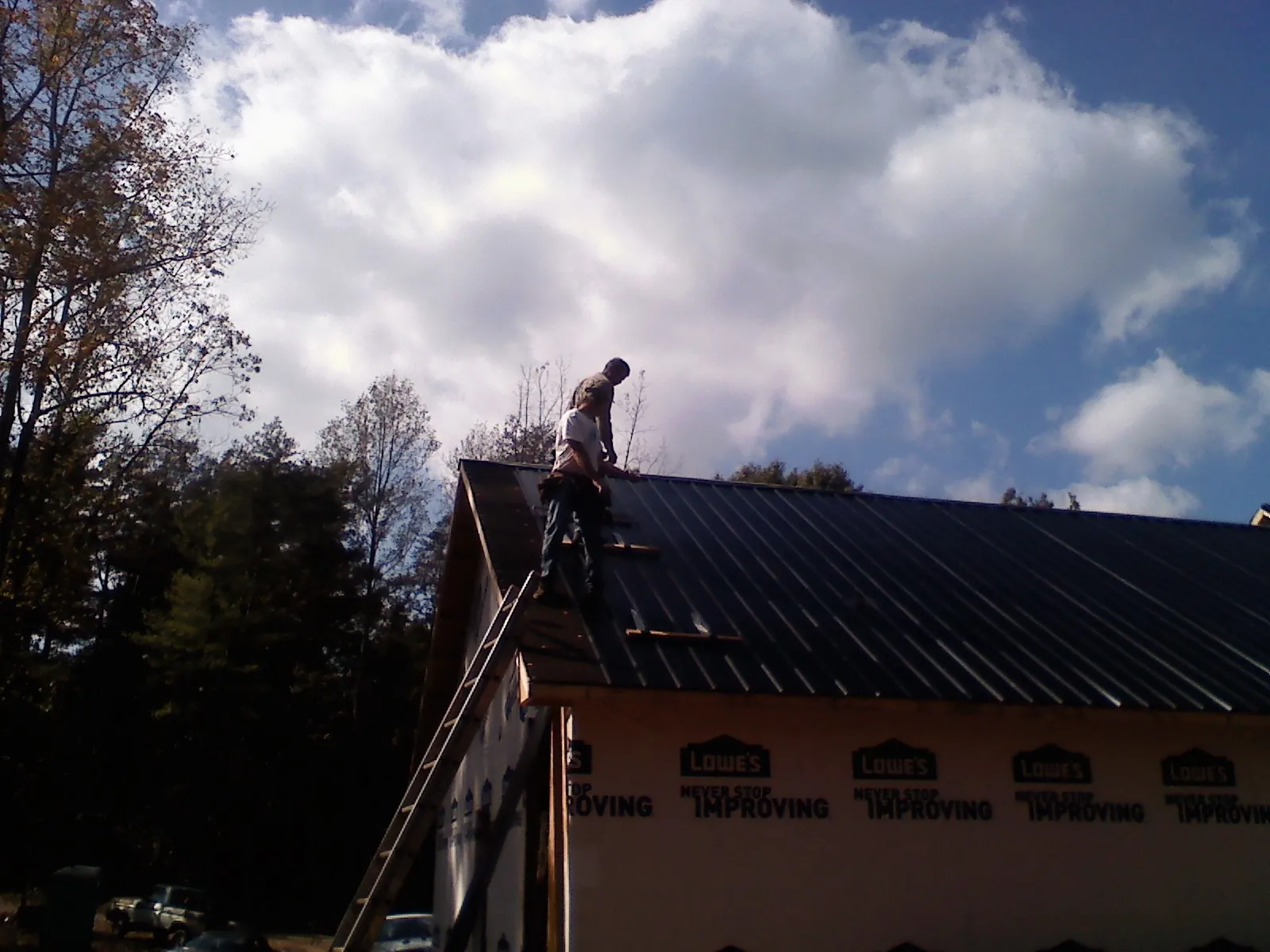 Roofer fastening dark metal panels high against a cloudy sky, from a Roof Inspection job in Covesville