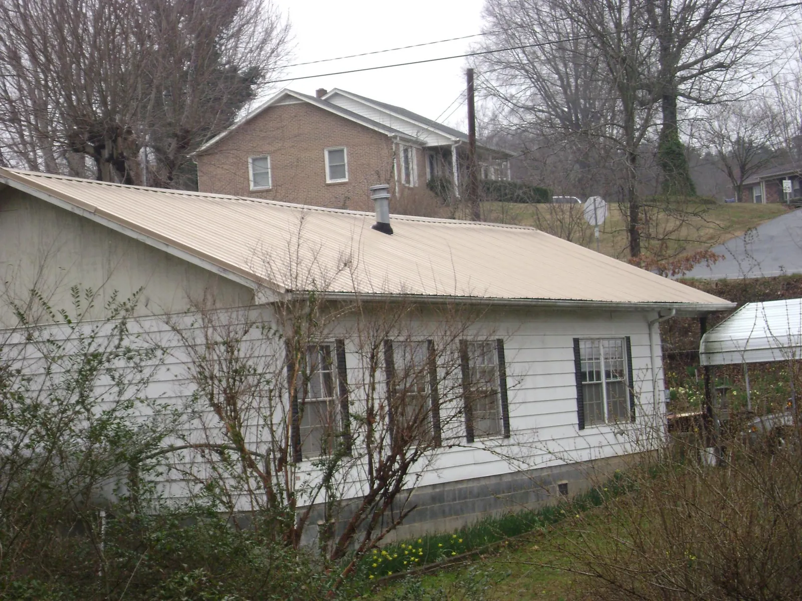 Tan metal roof on a white sided house set into a hillside — Commercial Roofing by Roofing Brothers in Covesville